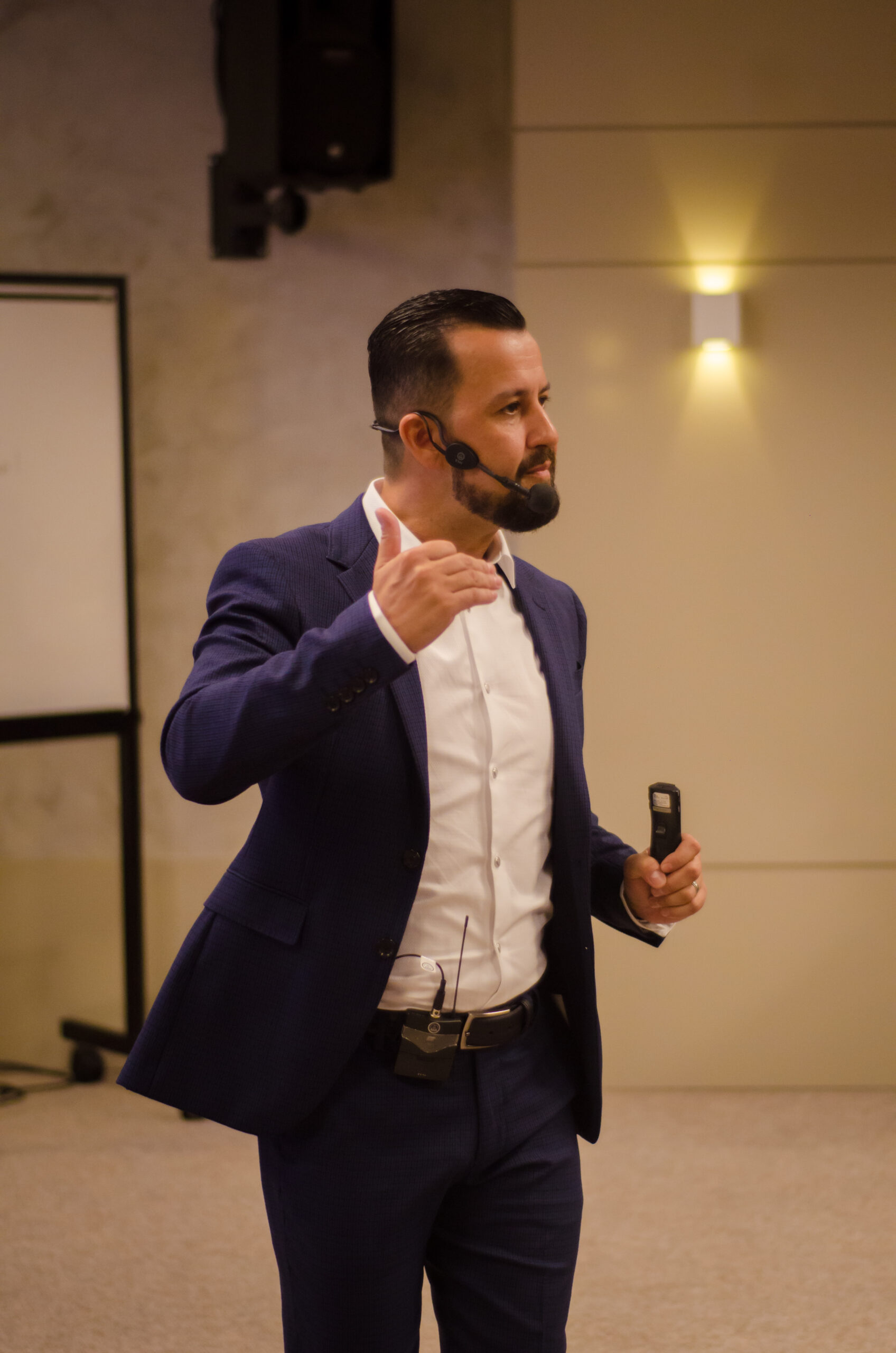 Cristovão Lucena de terno no palco conduzindo treinamento com microfone headset